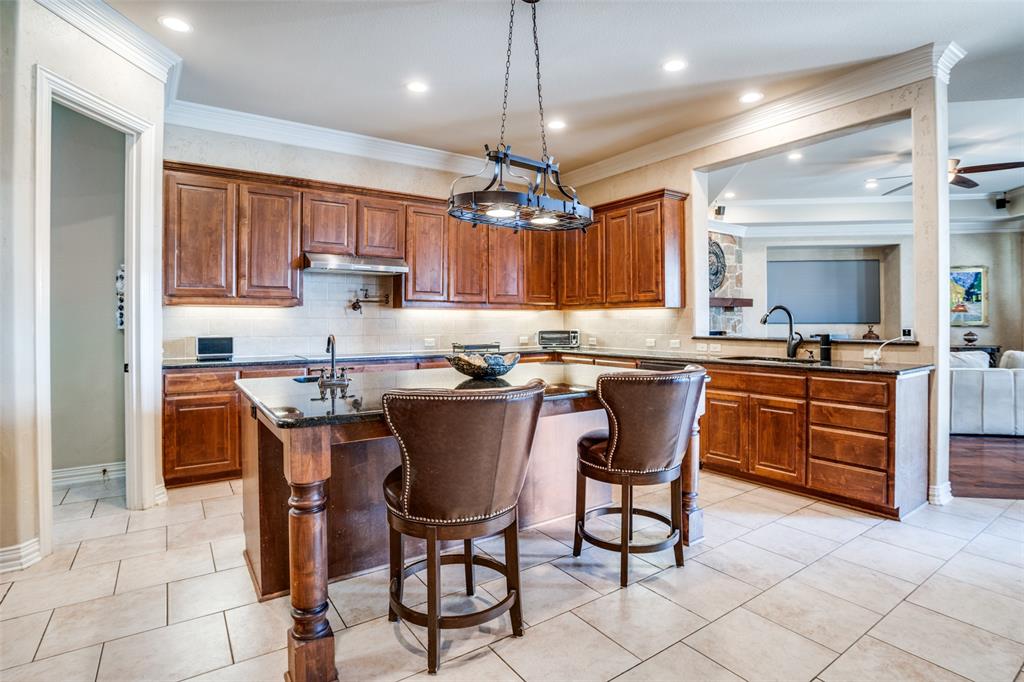 1929 Canyon Road Celina, TX 75009 - Photo 11 of 39 Kitchen with an island with sink, wood finish cabinets, decorative backsplash, a kitchen breakfast bar, and crown molding