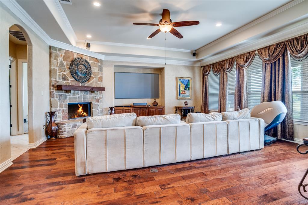 1929 Canyon Road Celina, TX 75009 - Photo 5 of 39 Living area with crown molding, a ceiling fan, arched walkways, a stone fireplace, and hardwood / wood-style floors