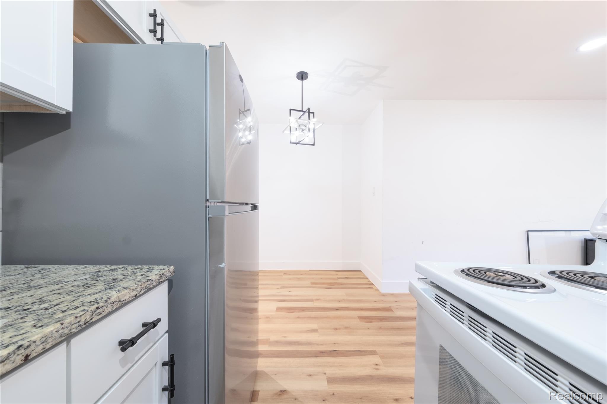 3065 South Commerce Road, Unit 9 Walled Lake, MI 48390 - Photo 8 of 15 Kitchenette featuring a stainless steel refrigerator, white cabinetry with dark hardware, granite-style countertops, wood-finish flooring, and a contemporary ceiling fixture