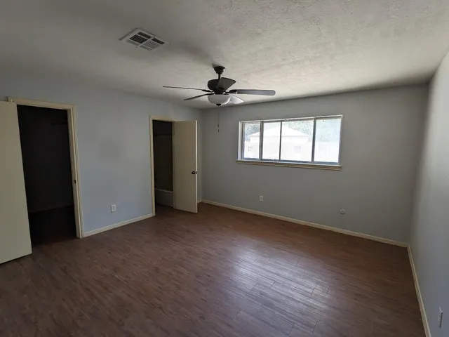 an empty room with wooden floor ceiling fan and windows