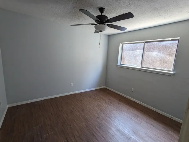 an empty room with wooden floor fan and windows