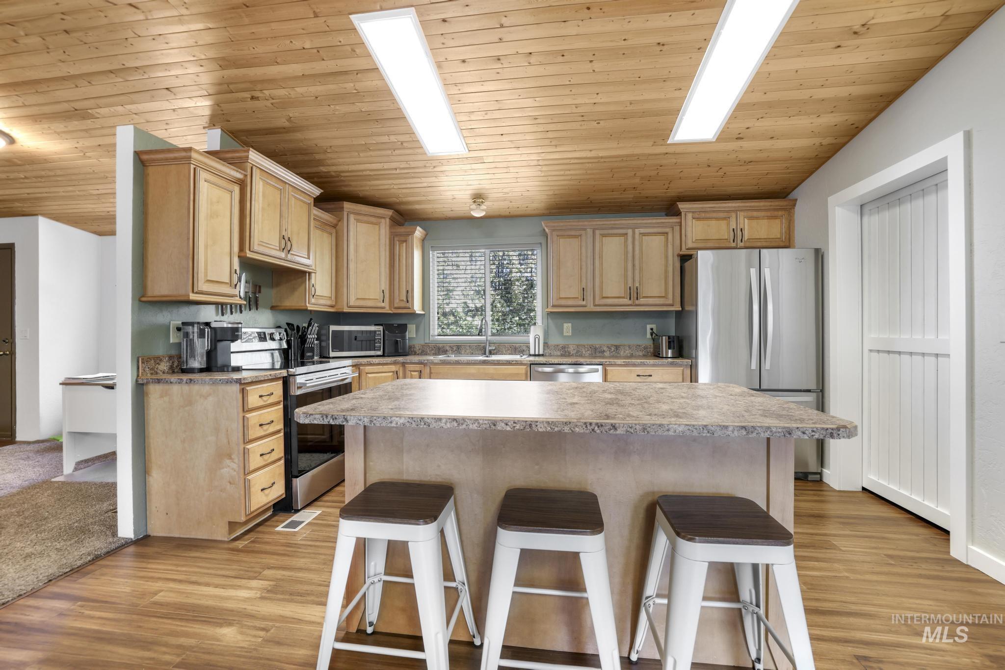 309 North Grape Street Shoshone, ID 83352 - Photo 5 of 26 Kitchen featuring a breakfast bar, light wood finish cabinetry, wooden ceiling, stainless steel appliances, and a center island