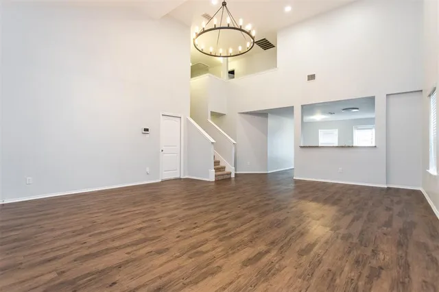a view of an empty room with wooden floor and kitchen view