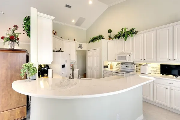 a kitchen with stainless steel appliances kitchen island granite countertop a white refrigerator a sink dishwasher and white cabinets with wooden floor