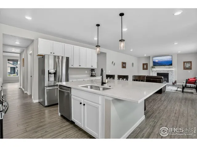 a kitchen with stainless steel appliances kitchen island granite countertop a refrigerator a stove a sink dishwasher and white cabinets with wooden floor