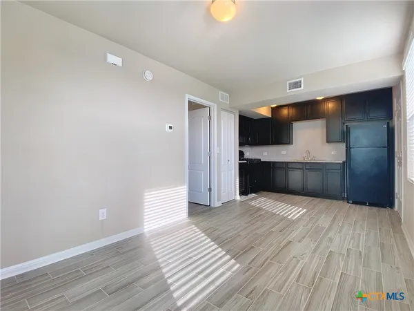 a view of empty room with wooden floor and kitchen