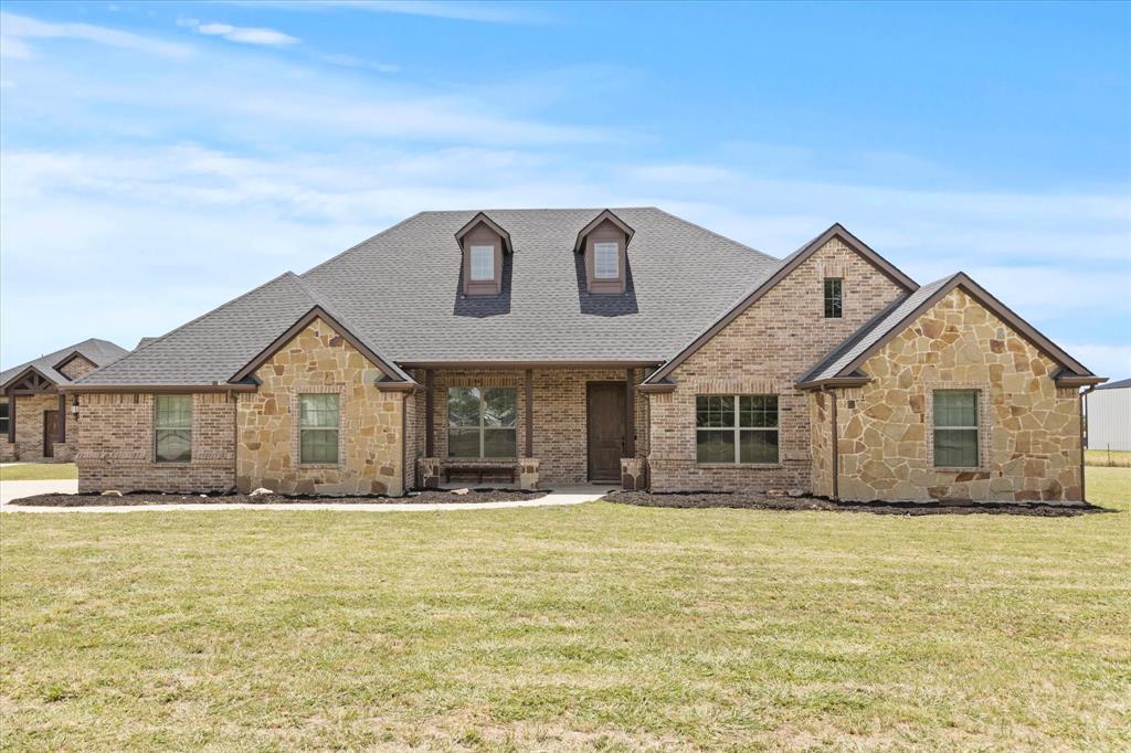 View of front of home featuring roof with shingles, stone siding, a front lawn, and brick siding