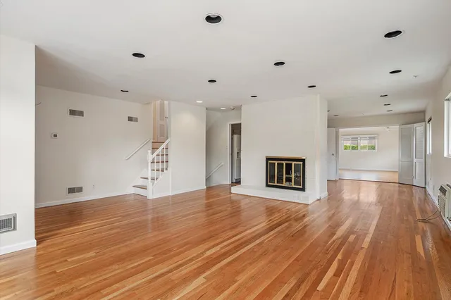 a view of an empty room with wooden floor and a kitchen