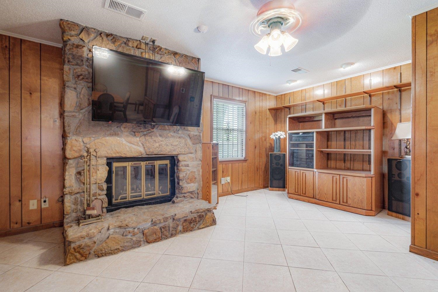5040 Warrington Road Memphis, TN 38118 - Photo 11 of 29 Unfurnished living room with wood walls, visible vents, ceiling fan, crown molding, and a stone fireplace
