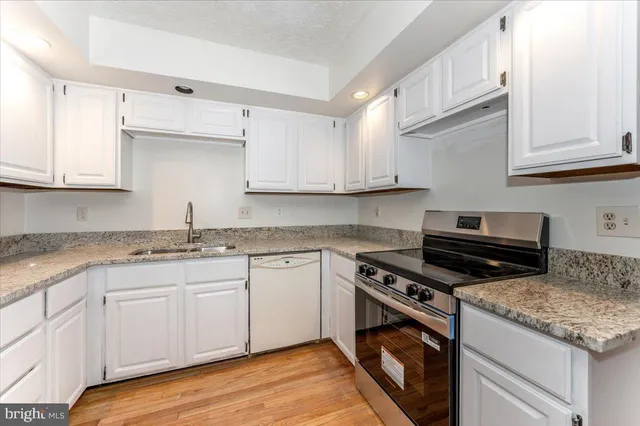 a kitchen with granite countertop white cabinets and a stove with wooden floor