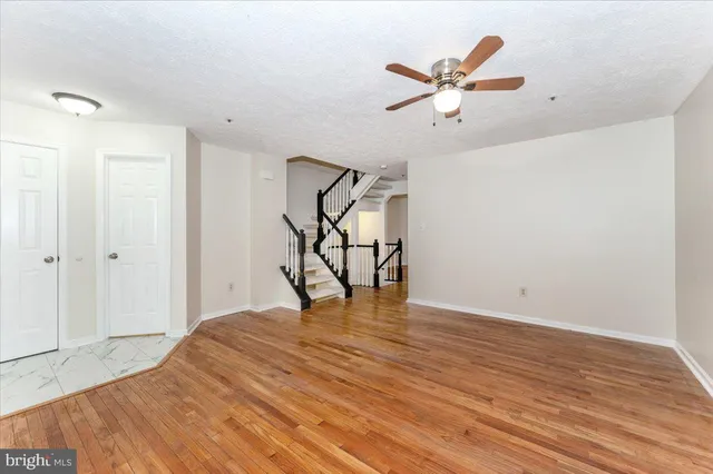 a view of an empty room with wooden floor and a ceiling fan