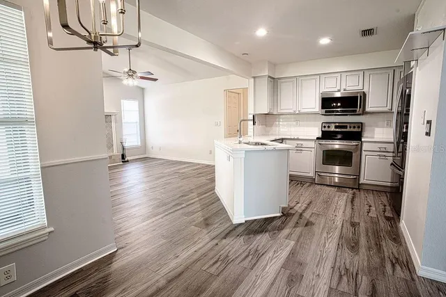 a kitchen with stainless steel appliances granite countertop a refrigerator a sink dishwasher a stove and white countertops with wooden floor