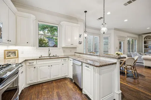 a kitchen with stainless steel appliances granite countertop a stove a sink dishwasher and white cabinets with wooden floor