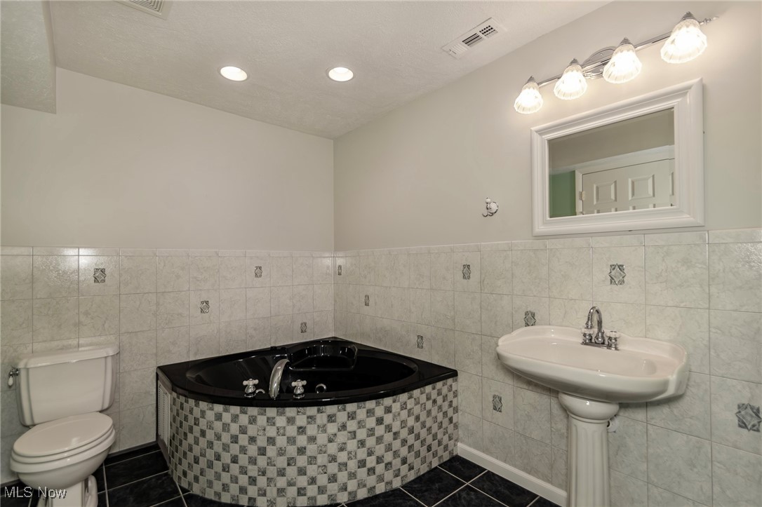 4815 South Ridge Road Perry, OH 44081 - Photo 35 of 48 Bathroom featuring tile walls, a bath, wainscoting, and dark tile patterned floors
