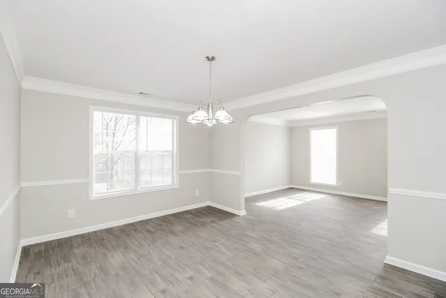 an empty room with wooden floor chandelier and windows