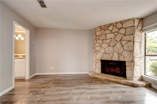 a view of an empty room with wooden floor and a fireplace