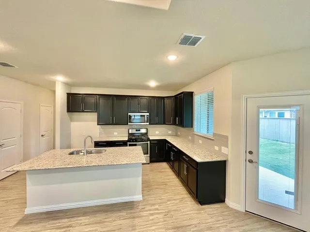 a large white kitchen with stainless steel appliances kitchen island a stove a refrigerator a oven and a sink with wooden floor