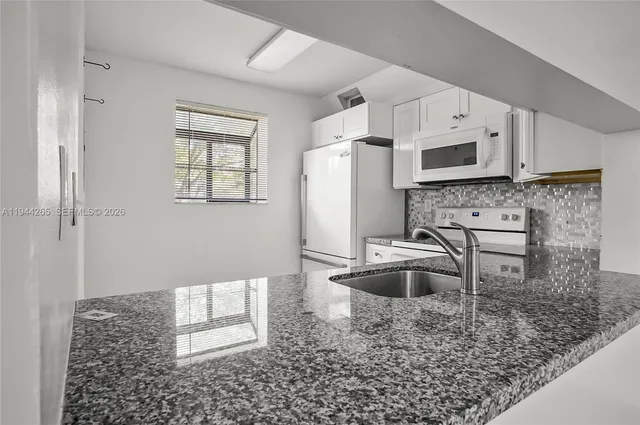 a kitchen with stainless steel appliances granite countertop a sink a stove a refrigerator a microwave with white cabinets and wooden floor