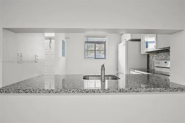 a kitchen with kitchen island granite countertop a sink and a refrigerator