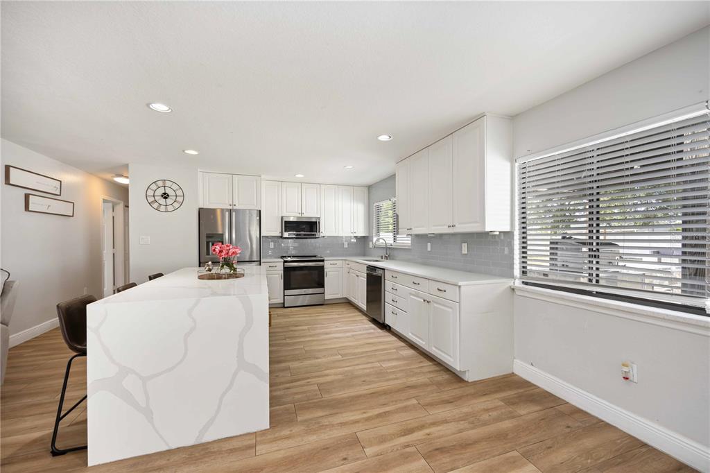 6775 Dennison Avenue North Port, FL 34287 - Photo 12 of 50 a large white kitchen with kitchen island a sink a stove and white cabinets next to a window