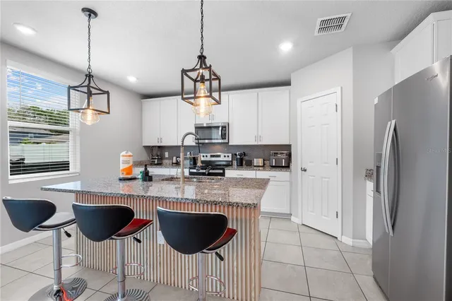 a kitchen with stainless steel appliances granite countertop a sink a stove a refrigerator and white cabinets with wooden floor