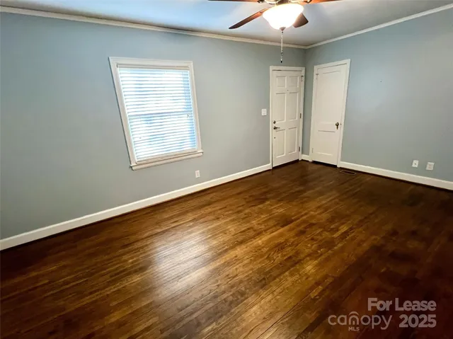 an empty room with wooden floor chandelier fan and windows