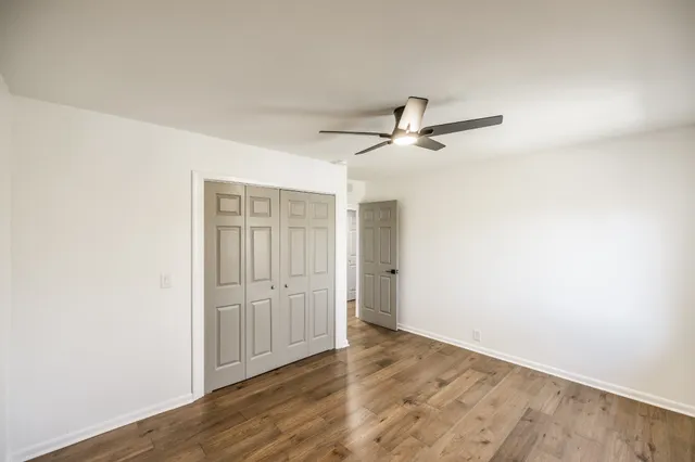 an empty room with wooden floor ceiling fan and windows