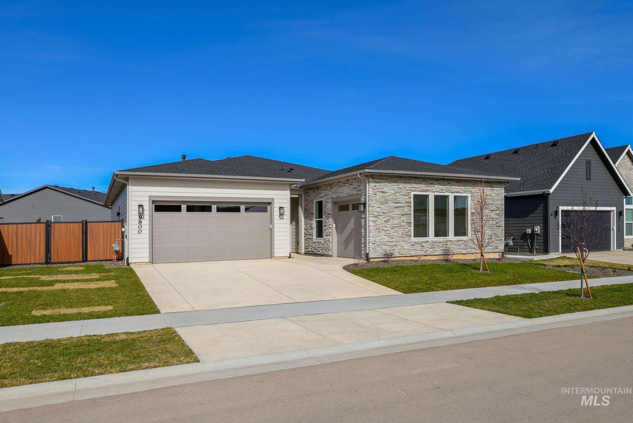 View of front facade featuring an attached garage, driveway, stone siding, and a shingled roof