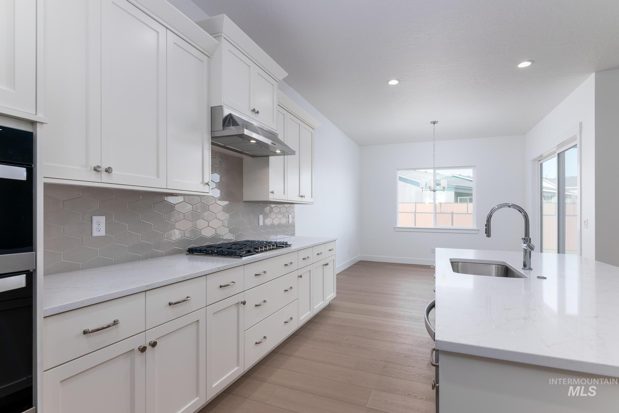 9800 West Novato Street Star, ID 83669 - Photo 11 of 40 Kitchen with white cabinets, light stone countertops, decorative backsplash, and light wood-style flooring