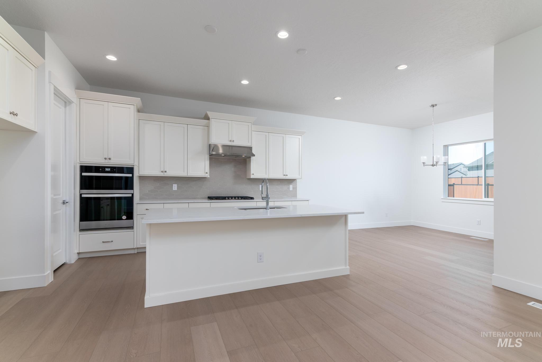 9800 West Novato Street Star, ID 83669 - Photo 9 of 40 Kitchen featuring white cabinets, a center island with sink, multiple ovens, a chandelier, and decorative backsplash