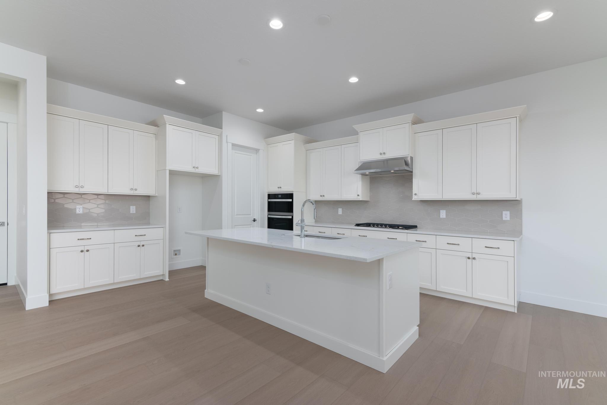 9800 West Novato Street Star, ID 83669 - Photo 10 of 40 Kitchen with white cabinets, decorative backsplash, a center island with sink, light wood-style floors, and recessed lighting