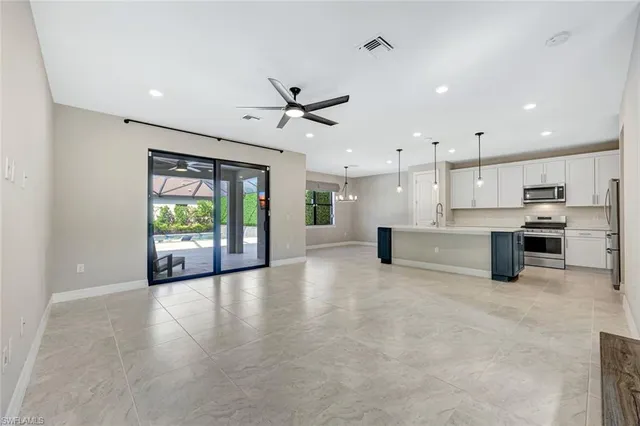 a view of an empty room with kitchen and window