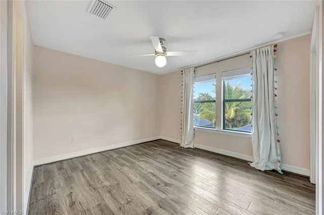 an empty room with wooden floor fan and windows
