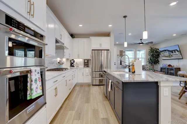 a kitchen with stainless steel appliances kitchen island granite countertop a stove top oven a sink dishwasher a refrigerator and a dining table with wooden floor