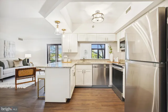 a kitchen with stainless steel appliances granite countertop a refrigerator a sink dishwasher a stove and white countertops with wooden floor