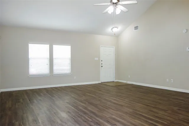 an empty room with wooden floor chandelier fan and windows
