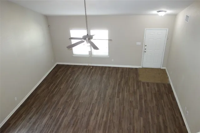 an empty room with wooden floor a ceiling fan and windows