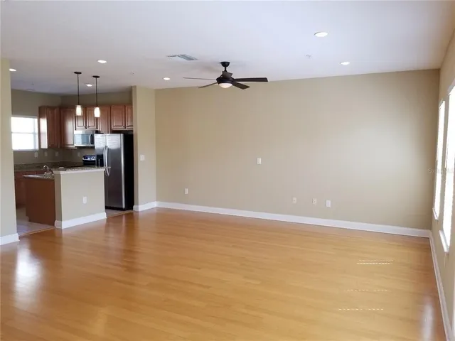 an empty room with wooden floor and kitchen view