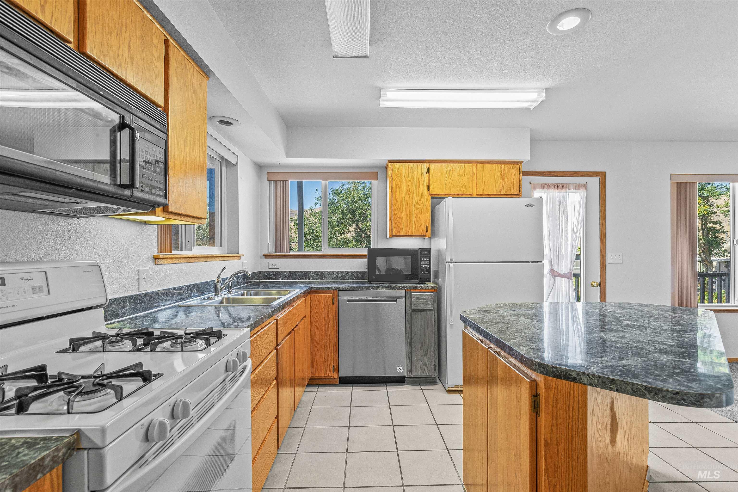 1962 Golfview Drive Clarkston, WA 99403 - Photo 15 of 34 Kitchen featuring white appliances, a center island, light tile patterned flooring, and brown cabinetry