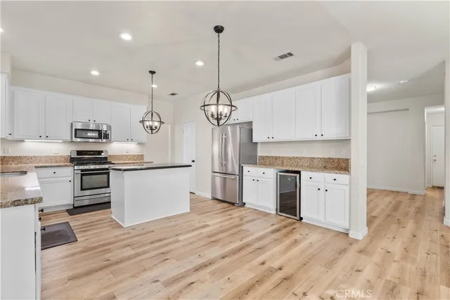 a kitchen with stainless steel appliances kitchen island granite countertop a refrigerator a sink dishwasher a stove and white cabinets with wooden floor