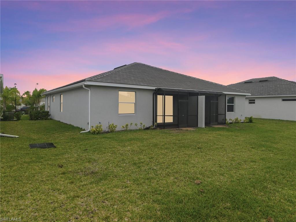 2220 Dragonfruit Way Naples, FL 34120 - Photo 26 of 31 Rear view of house featuring a lawn, stucco siding, and a sunroom