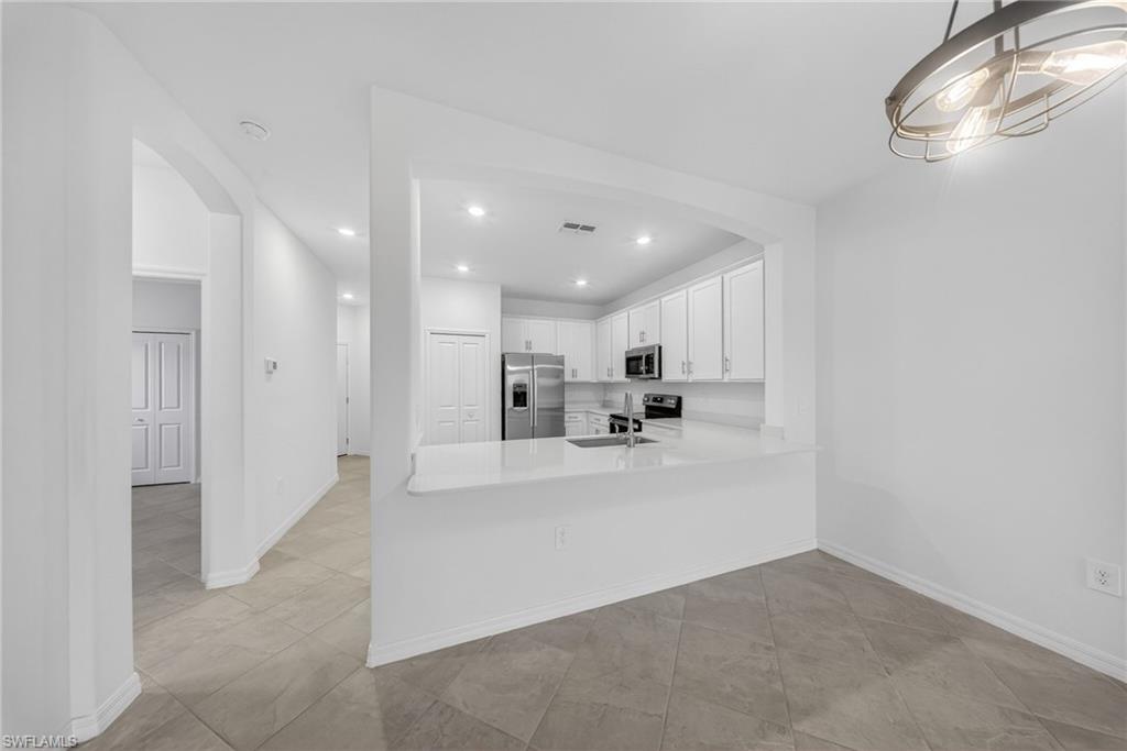 2220 Dragonfruit Way Naples, FL 34120 - Photo 4 of 31 Kitchen with arched walkways, white cabinets, stainless steel appliances, a peninsula, and light stone countertops