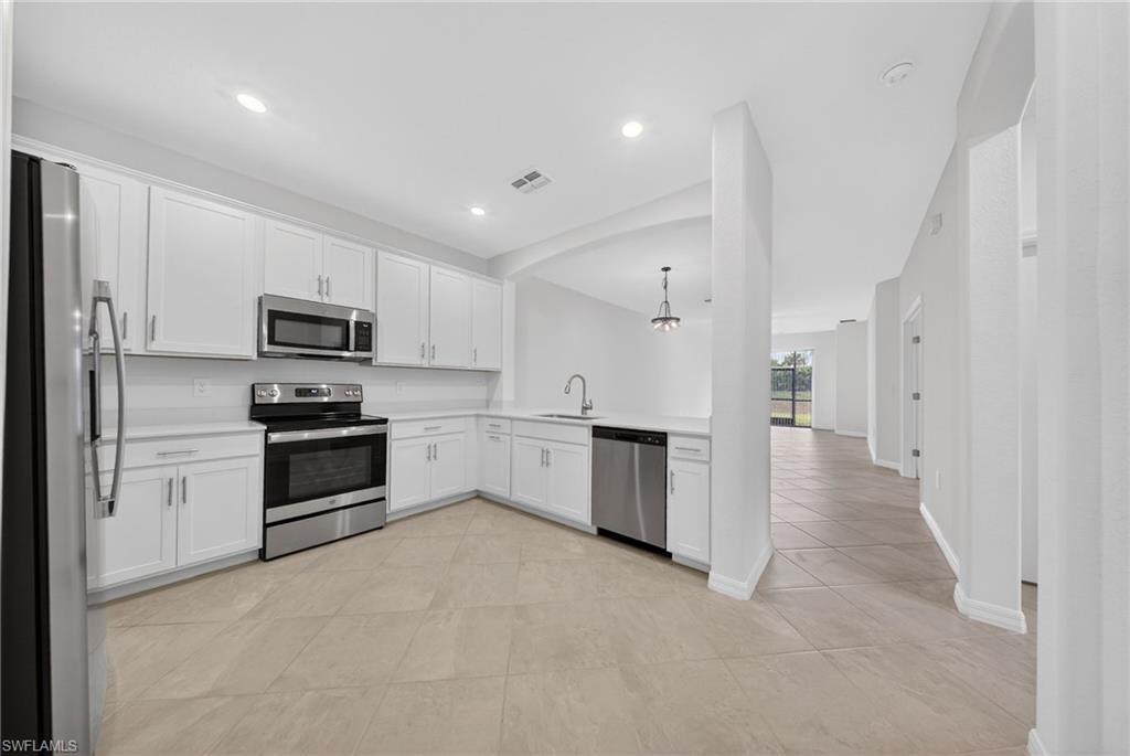 2220 Dragonfruit Way Naples, FL 34120 - Photo 5 of 31 Kitchen with white cabinetry, stainless steel appliances, light countertops, light tile patterned floors, and a peninsula
