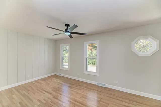 a view of empty room with wooden floor and fan