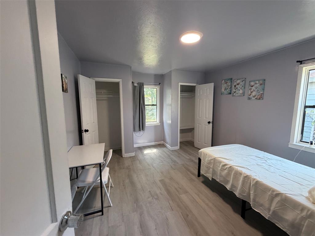 513 Shawnee Trace Grand Prairie, TX 75051 - Photo 21 of 32 Room with light grey walls, wood-finish flooring, two windows with grey curtains, and two closet spaces with bifold doors