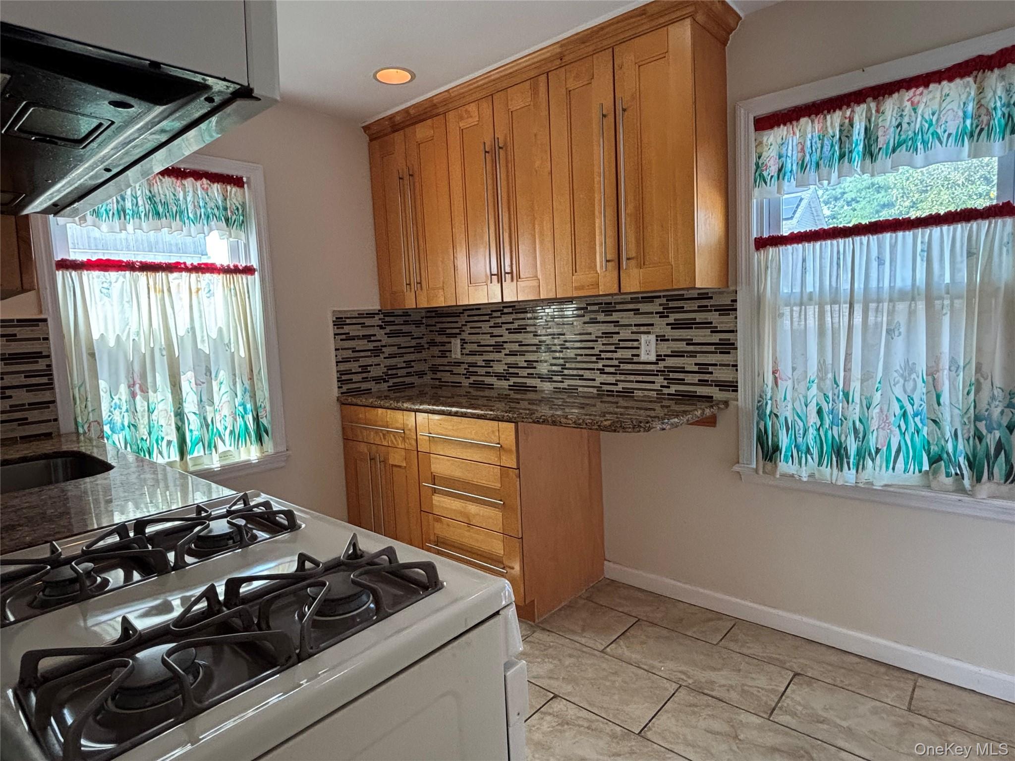 104-18 216th Street Queens, NY 11429 - Photo 18 of 49 Kitchen featuring white range with gas cooktop, extractor fan, brown cabinets, decorative backsplash, and dark stone countertops