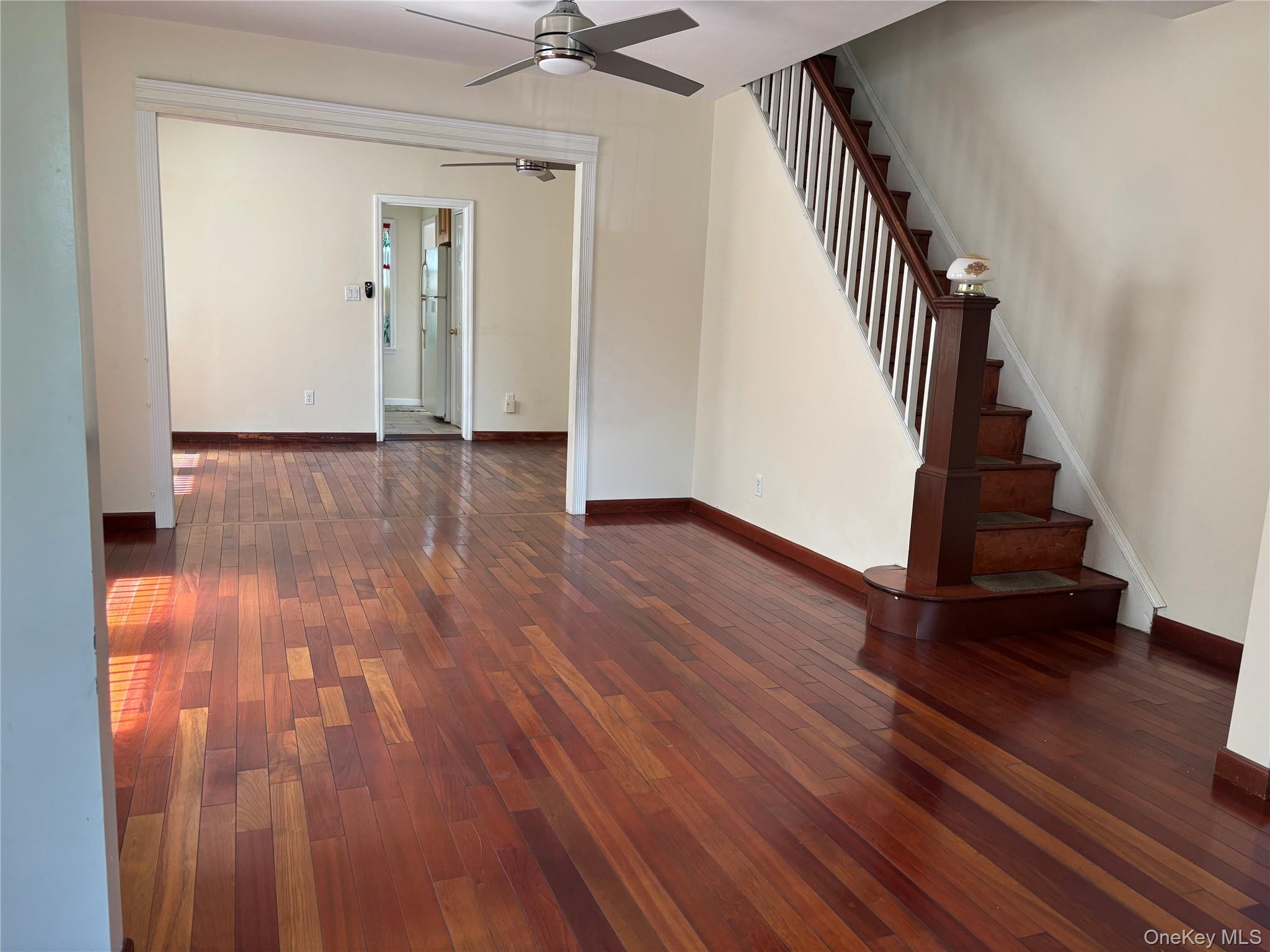 104-18 216th Street Queens, NY 11429 - Photo 10 of 49 Unfurnished living room with dark wood finished floors, ceiling fan, and stairway