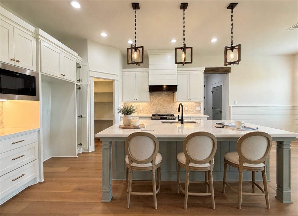 3245 Hunters Crossing Bryan, TX 77808 - Photo 7 of 30 Spacious kitchen featuring a large central island with a light-toned countertop, white shaker-style cabinetry, stainless steel microwave, wood-finish flooring, and a walk-in pantry