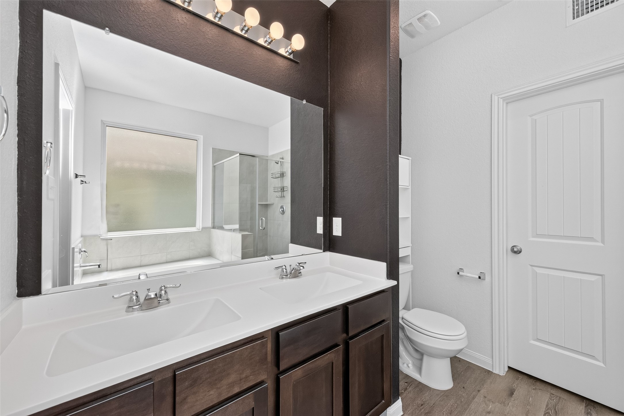 2526 Sturgeon Way Conroe, TX 77384 - Photo 23 of 49 This bathroom features a modern double vanity with dark wood cabinets, a large mirror, and overhead lighting. It includes a glass-enclosed shower, a separate bathtub, and a toilet with a privacy door. The space is brightened by natural light from the frosted window.