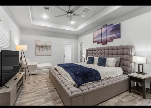 a spacious bedroom with a bed a couch and a flat tv screen on dresser